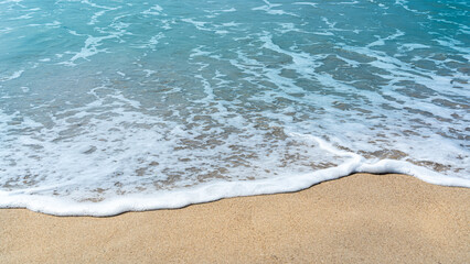 soft, foamy ocean waves gently roll onto a light tan sandy beach, creating a peaceful and serene coastal scene.
