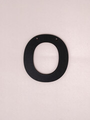 Wooden black letter O on a gray background with holes for a rope
