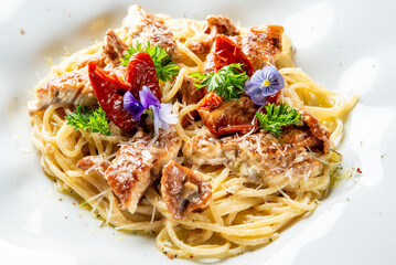 Spaghetti with grilled meat, sun-dried tomatoes, parsley, edible flowers, and grated cheese on a white plate. Gourmet pasta dish with vibrant colors