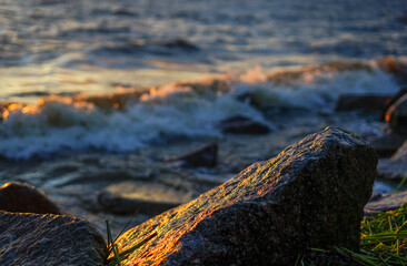 Fototapeta premium Waves crash against the rocky seashore at sunset