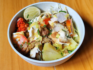 A bowl of Indonesian chicken soto with shredded chicken, sliced boiled egg, vermicelli, sliced...