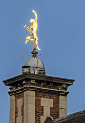 Golden statue of Mercury, the Roman god of commerce and communication, standing atop a classical brick and stone building. The figure is shown in motion with winged feet and a caduceus,  in Lille, Fra