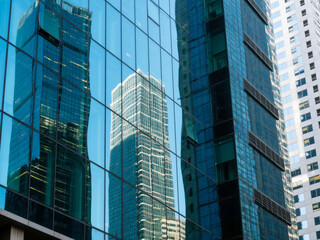 Obraz premium Tall skyscrapers reflected on the glass facade of a modern office building in the city. Perfect for use in corporate presentations, financial services, real estate advertising, business growth