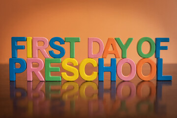 Wooden blocks spell FIRST DAY OF PRESCHOOL on orange background, warm glow, sharp focus