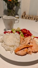 Grilled salmon served with white rice, avocado salad, and a cup of tea on a clean white table