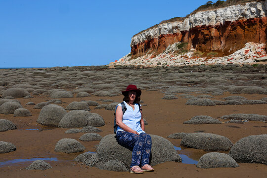 Woman sitting on a rock on the beach, with historic red cliffs from the costal erosion, and blue sky