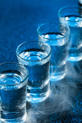 Wet glasses of vodka in smoke on dark blue background.