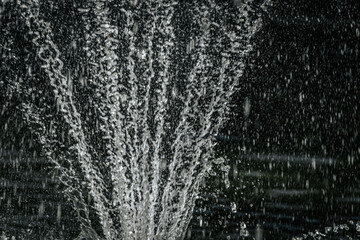 Abstract close-up of falling water droplets, captured in motion against a dark background, creating a textured and dynamic pattern.