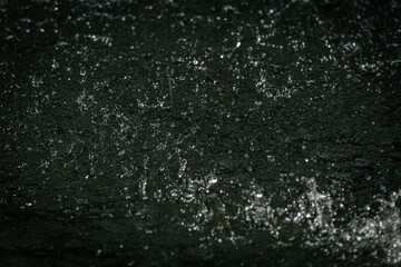 raindrops splashing on water, capturing droplets and ripples in motion with a dramatic, dark background.