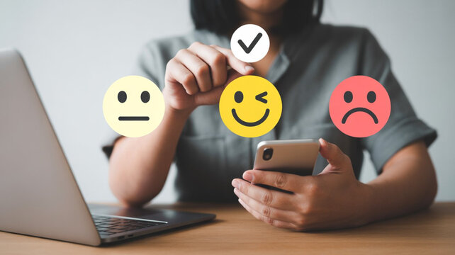 Woman selects happy emoji with checkmark on smartphone screen with laptop nearby customer feedback