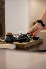 Hand Pouring Hot Tea from a Black Teapot