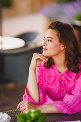 Fototapeta premium Beautiful brunette young woman in bright pink dress at summer cafe table. 