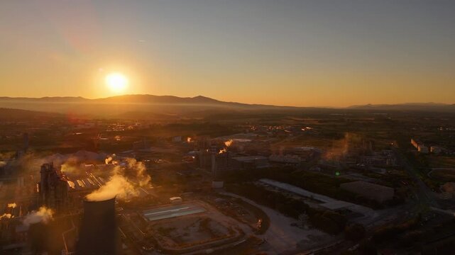 Drone aerial view of massive industrial factory with smokestacks, sprawling grounds, machinery and production lines at sunset, emphasizing industrial scale and power