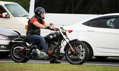 Fototapeta premium Biker in leather vest riding motorcycle on a busy road during daytime near parked cars