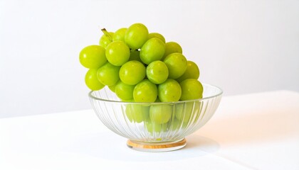 A beautiful bunch of fresh, ripe green grapes sitting in a clear glass bowl against a clean white background, a concept of healthy food.