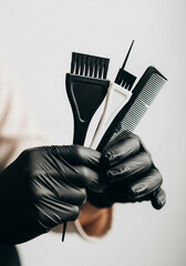 Gloved hand holding hair coloring brushes and comb