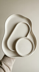 Three organic shaped white ceramic plates stacked on a hand