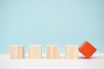 Wooden blocks neatly aligned on a surface, with one painted red and tipping to represent individuality, contrast, or change against uniformity in business, education, or creative projects.