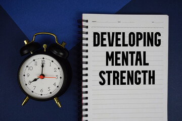 Developing Mental Strength text written on notepad with alarm clock on blue background