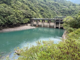 Fototapeta premium A concrete dam with waters lies in the heart of a lush green valley bordered by forested hills blending human engineering with natural beauty for themes of sustainability, water resources and nature