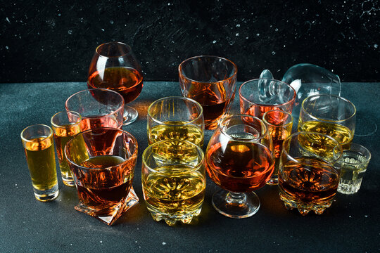 A set of glasses with various alcoholic beverages: vodka, cognac, tequila, scotch, brandy and whiskey, grappa, liqueur, vermouth, tincture, rum. Strong alcoholic drinks. On a stone background.