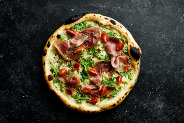 Traditional pizza with prosciutto, cherry tomatoes, arugula and cheese. Takeaway food. On a black stone background. Rustic style.