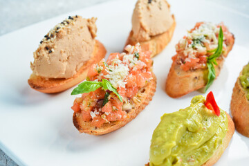 Set bruschetta. Sandwiches with avocado, liver pâté and vegetables. On a white plate. On a gray stone background. Restaurant menu.
