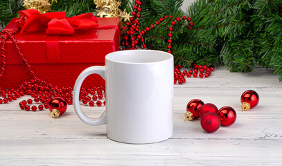 White mug standing on white wooden table with christmas decorations and red gift box