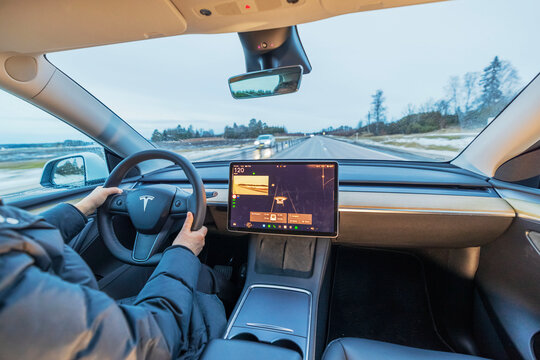 Tesla Model Y electric car interior with driver on highway, central touchscreen showing 360-degree camera view and navigation. Sweden. 