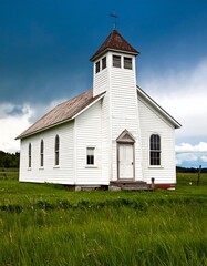 Fototapeta premium White clapboard church in a grassy field under a partly cloudy sky