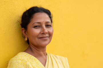 indian woman in traditional sari radiating warmth and friendliness sits against ultrabright yellow background
