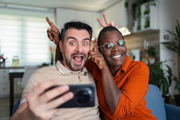 Playful couple taking a selfie making funny faces at home