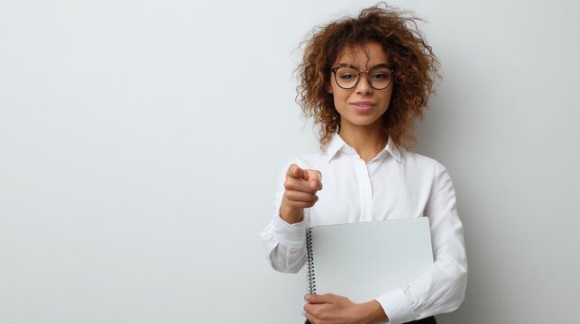 Confident Professional's Assertive Gaze: A sophisticated businesswoman with spectacles and a warm gaze, confidently pointing at the viewer while clutching a laptop, embodies poise and professionalism.