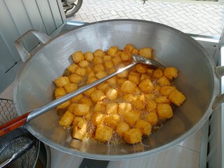 Tahu crispy or Golden crispy tofu cubes are being deep-fried in a large pan filled with hot oil, showing a delicious street food snack with crunchy texture and appetizing golden color.