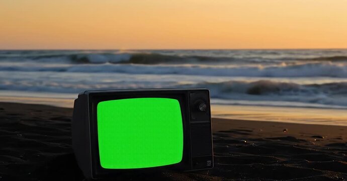 Vintage TV with a green screen on a beach at sunset with ocean waves.