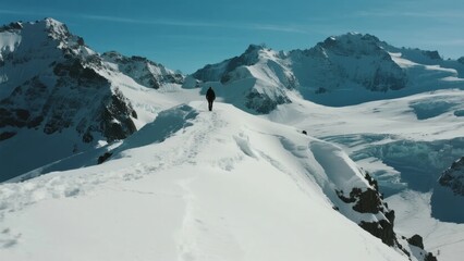 Fototapeta premium Solo Hiker on Snow-Capped Mountain Ridge Under Clear Blue Sky