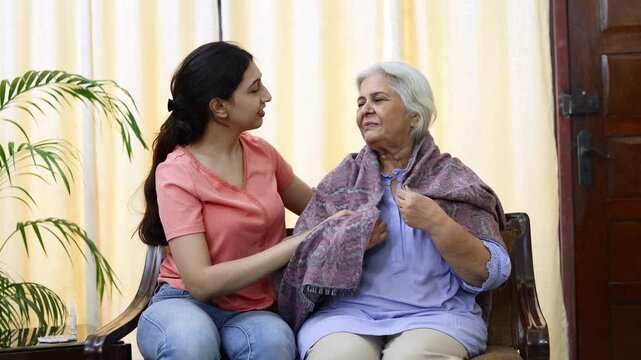 Young indian granddaughter covering her sick grandmother with warm woolen blanket at home. Elderly care. 4k