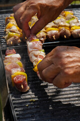 A close-up of meat and vegetable skewers on a smoking grill. A hand with tongs turns the food, with thick steam creating a dynamic, hazy atmosphere. The photo captures the lively process of grilling