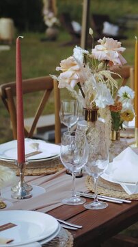 Vertical video. Wedding table setting with candles, dried flowers and pastel flowers. Outdoor boho style party, plates and glasses, no people or food.
