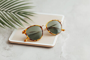 Summer vibes stylish sunglasses on a tablet with a plant in a vase on a marble table surrounded by a wooden board in a relaxing environment
