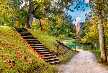 Golden autumn in old public  park with pedestrians walkways, stairs on the hills, pond or  lake and medieval tower at the distance