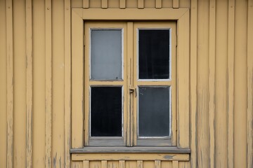 Weathered yellow wooden wall with a vintage four-pane window, showing rustic charm and textured detail