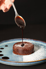 Main féminine versant du chocolat coulant sur un fondant au chocolat saupoudré de sucre glace