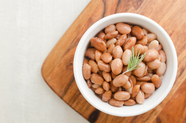 Boiled borlotti beans in a white bowl on a wooden cutting board on a gray background. Italian cuisine. Vegan and vegetarian food. Selective focus. Horizontal orientation. Copy space. Top view