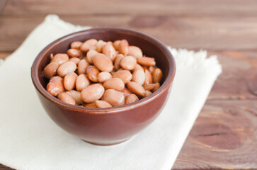 Boiled borlotti beans in a brown bowl on a napkin on a wooden background. Italian cuisine. Vegan and vegetarian food. Selective focus. Horizontal orientation. Copy space.