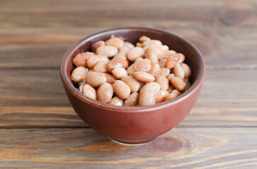 Boiled borlotti beans in a brown bowl on a wooden background. Italian cuisine. Vegan and vegetarian food. Selective focus. Horizontal orientation. Copy space.