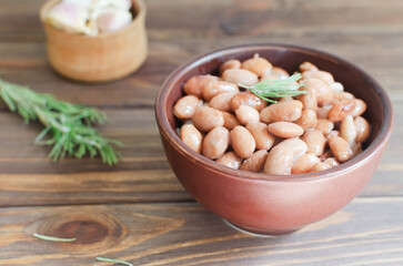Boiled borlotti beans in a brown bowl with rosemary and garlic on a wooden background. Italian cuisine. Vegan and vegetarian food. Selective focus. Horizontal orientation.