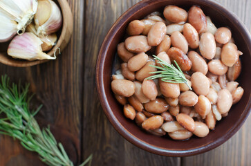 Boiled borlotti beans in a brown bowl with rosemary and garlic on a wooden background. Italian cuisine. Vegan and vegetarian food. Selective focus. Horizontal orientation. Top view