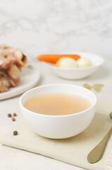 Veal bone broth in a white bowl with ingredients on a white table. Collagen concept. Selective focus. Vertical orientation. Copy space