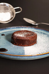 Fondant au chocolat saupoudré de sucre glace avec cuillère et saupoudreuse en arrière-plan
